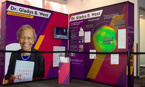 Exhibit honoring Dr. Gladys B. West, featuring biography, a book titled "Hidden Figures," and a colorful geoid model. The tone is informative and celebratory.