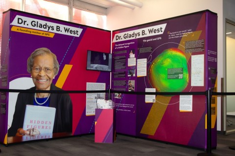Exhibit honoring Dr. Gladys B. West, featuring biography, a book titled "Hidden Figures," and a colorful geoid model. The tone is informative and celebratory.