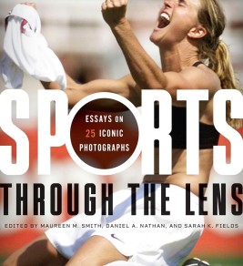A woman athlete celebrates passionately on a field, holding her jersey in the air. The cover of a book titled "Sports Through the Lens" overlays the image.